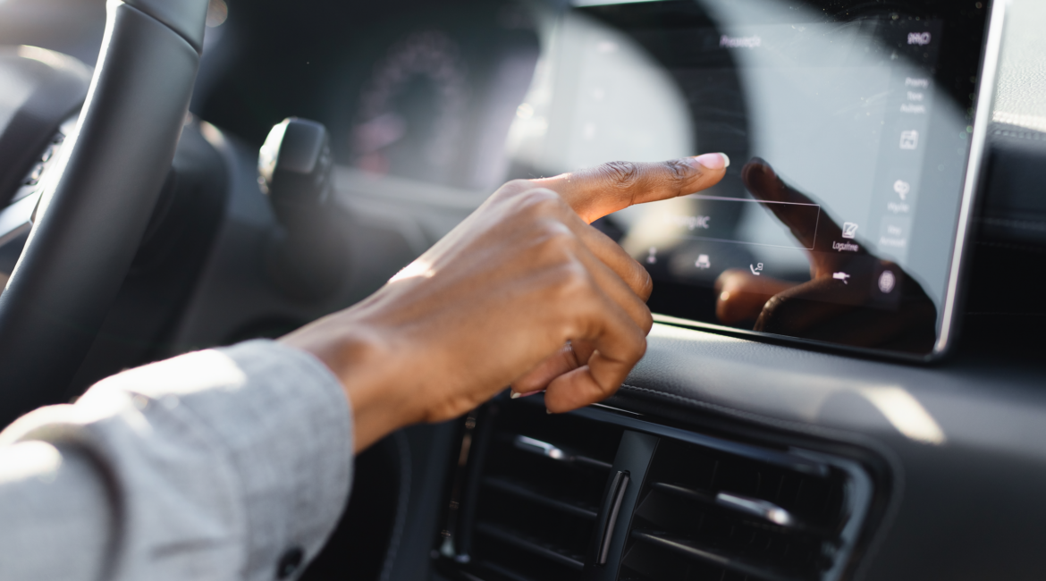Driver's hand reaching out to tap the touchscreen on a car dashboard in warm daylight