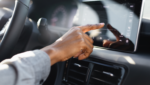 Driver's hand reaching out to tap the touchscreen on a car dashboard in warm daylight