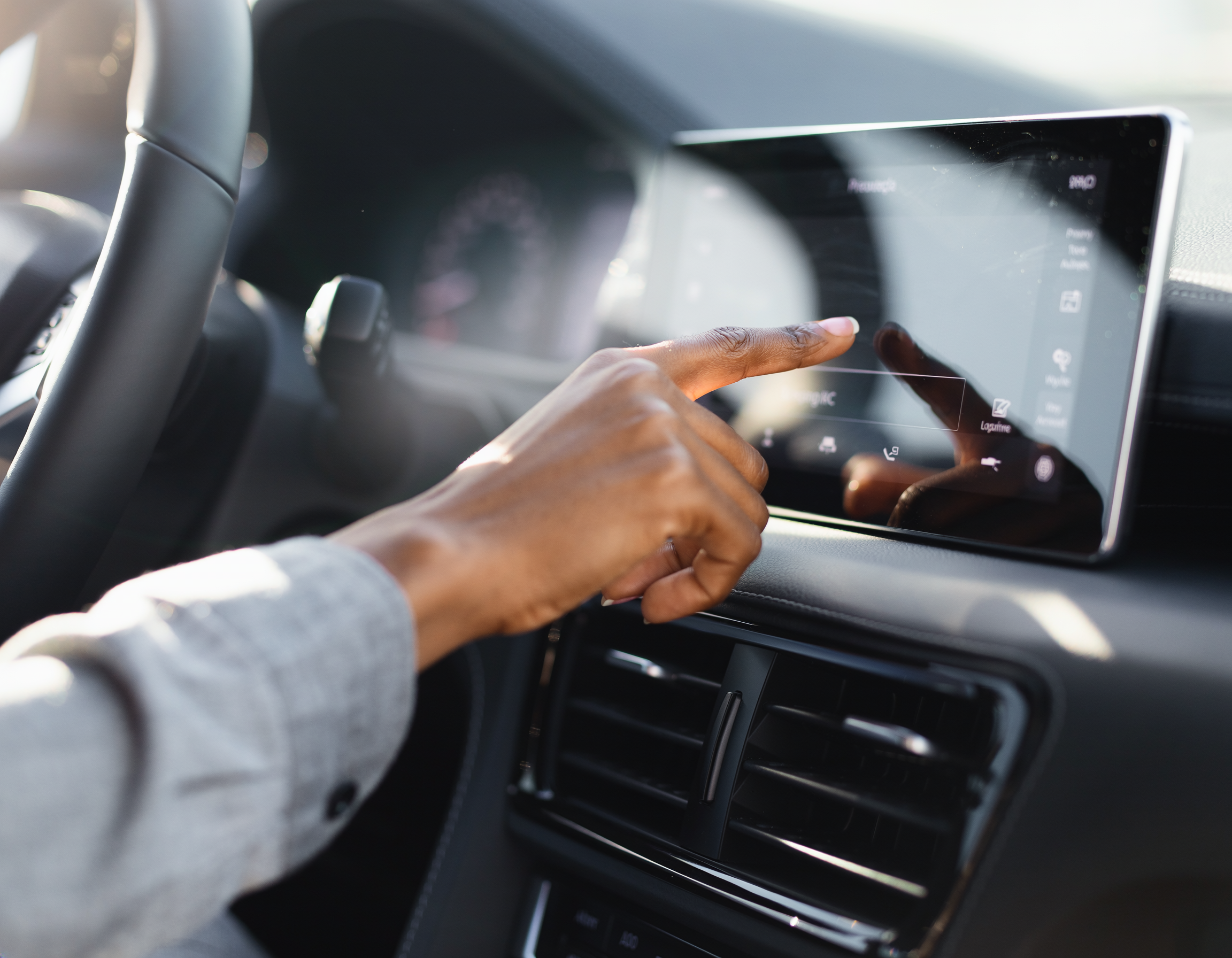 Driver's hand reaching out to tap the touchscreen on a car dashboard in warm daylight