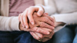 Adult daughter sits beside her elderly father at home, holding his hand during a serious conversation